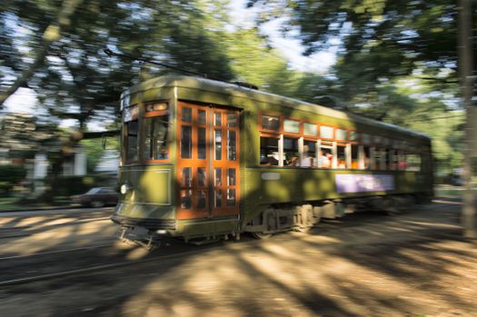 A green trolley moving down the center of a tree-lined street in New Orleans.