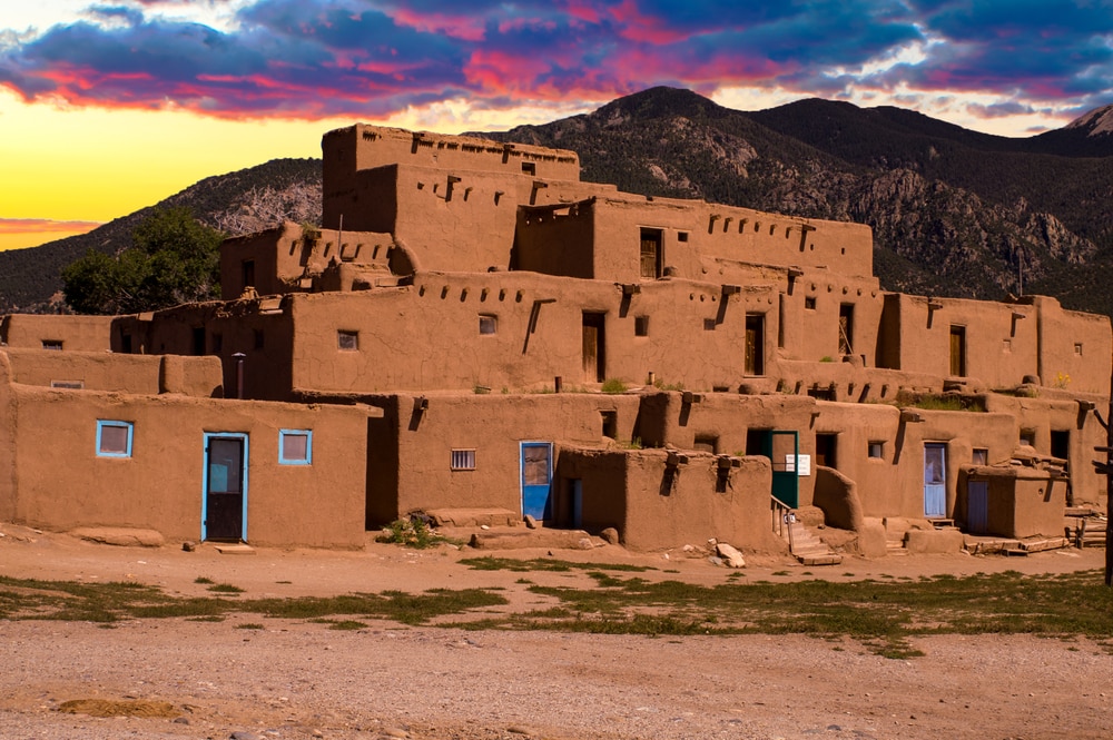Taos Pueblo at sunset with incredible colors staining the dark clouds.