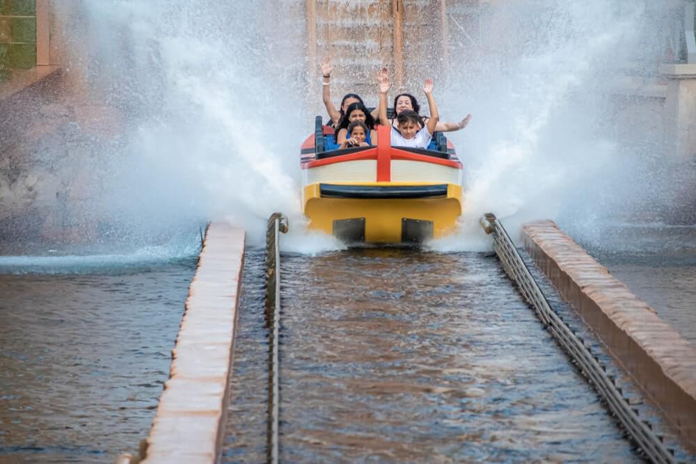 People lifting up their hands at a water ride at a theme park.